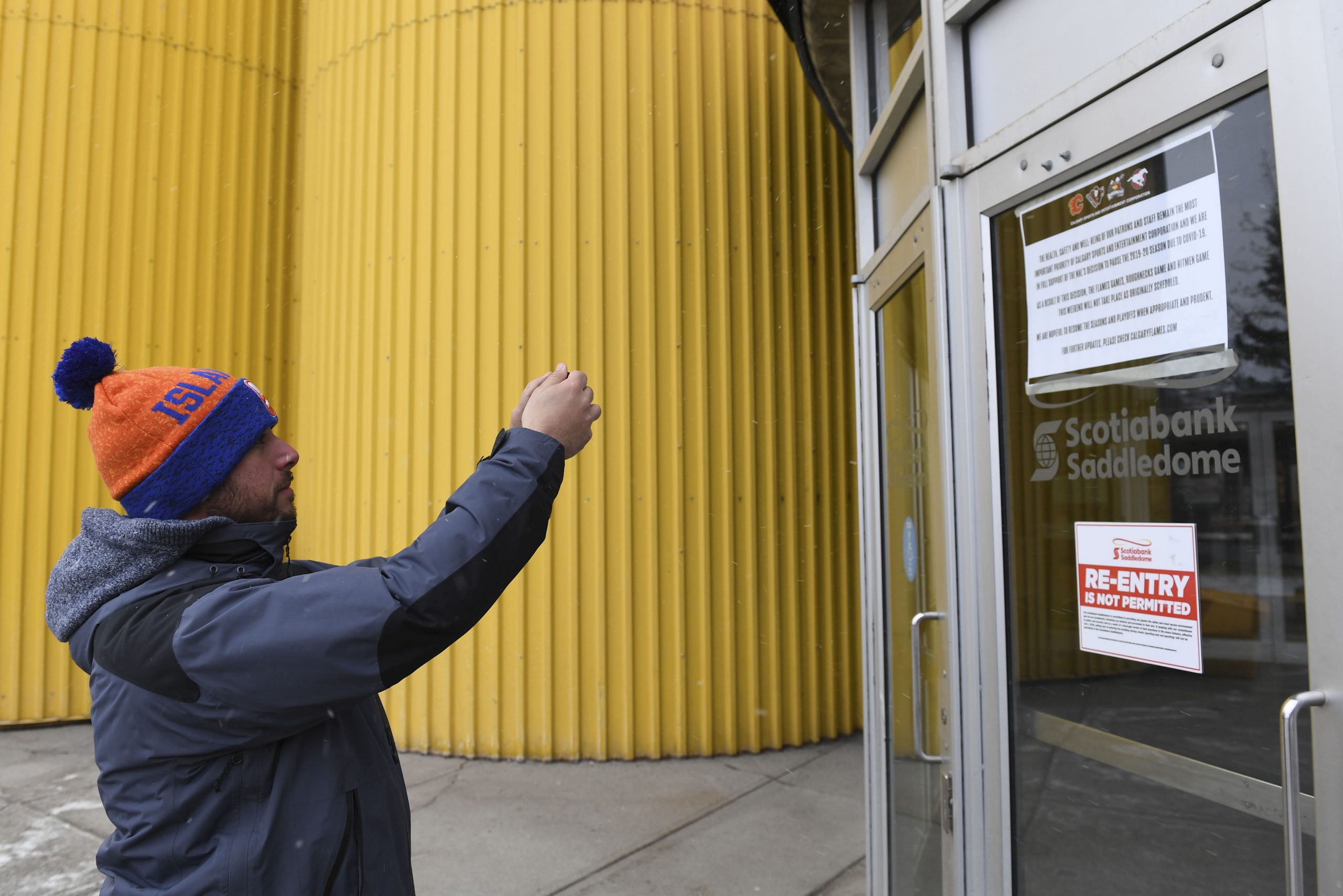 Mar 12, 2020; Calgary, Alberta, CAN; Joe Cosmo, from Long Island, NY takes a photo of the closure notice at the Scotiabank Saddledome after the announcement by the NHL of the suspension of NHL play due to the coronavirus. Cosmo travelled from New York to see the Islanders play the Flames on Wednesday night as part of his goal to see the Islanders play in all 31 NHL arenas. Mandatory Credit: Candice Ward-USA TODAY Sports