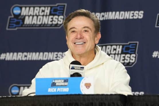 Iona Gaels head coach Rick Pitino smiles at the podium.