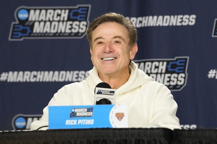 Iona Gaels head coach Rick Pitino smiles at the podium.