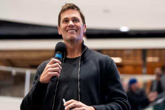 Tom Brady holds a mic up to his face.